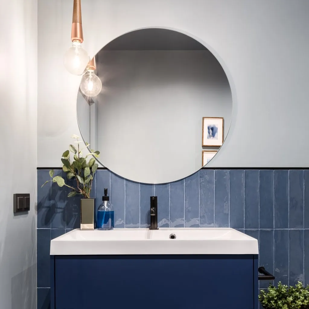 Designed bathroom with stylish blue cabinet, blue wall tiles and big round mirror