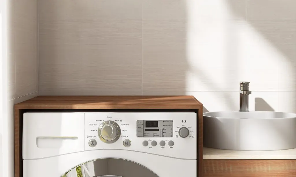 Blank space on brown wooden countertop counter in laundry room, washing machine, cabinet, white washbasin in sunlight, soft window shadow on cream tile wall in background 3D