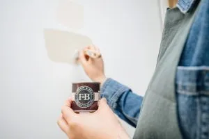 Paris, France - May 30, 2020: Woman painting with Farrow and Ball sample pot new colour on her wall during reconstruciton of the house apartment